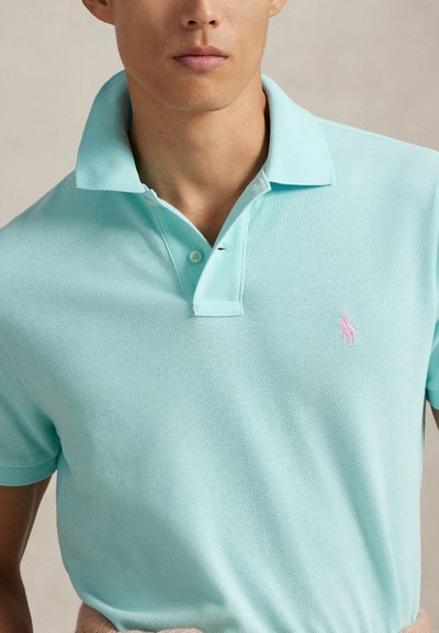 Ανοιχτό μπλε πόλο μπλούζα με υφασμάτινη υφή, κλασικό γιακά και μικρό ροζ λογότυπο στο αριστερό μέρος του στήθους. Κοντά μανίκια και άνετη εφαρμογή.