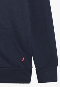 Mörkblå sweatshirt gjord av bomullsblandning. Har en framficka, ribbade ärmslut och en liten röd logotagg på sidan.