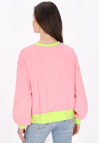Felpa rosa con vestibilità morbida, caratterizzata da un colletto e un orlo a coste di colore verde neon. Tessuto liscio con maniche a palloncino, senza motivi visibili.