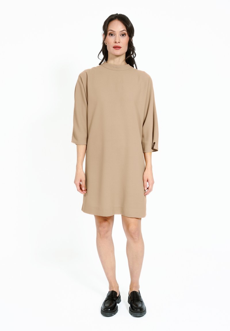 Rochie bej, de lungime midi, cu guler înalt și mâneci șapte, confecționată dintr-un material neted. Asortată cu pantofi negri, cu talpă groasă, slip-on.