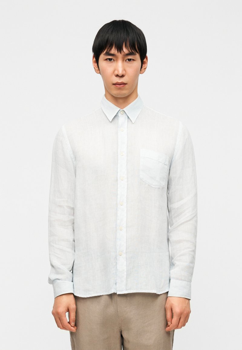 Ανοιχτόγαλάζιο πουκάμισο με μακριά μανίκια από διάφανο ύφασμα, με γιακά με κουμπιά, τσέπη στο στήθος και κουμπιά ανοιχτού χρώματος.