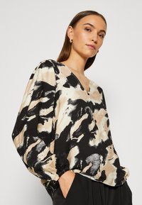Blusa leggera e stampata con scollo a V, maniche lunghe con polsini elastici, nei toni di beige, nero e bianco. Tessuto testurizzato.