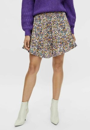 Rock mit Blumenmuster in Schwarz, Lila und Gelb, mit Plisseefalten und elastischem Bund, kombiniert mit weißen Stiefeletten.