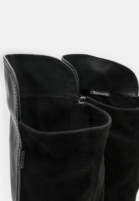 Stivali in pelle nera e suede con punta arrotondata, dotati di chiusura con cerniera e dettagli cuciti. L'interno è rivestito con un tessuto morbido.