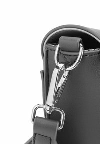 Detail šedé faux kůže tašky s kovovou sponou a kroužkovým upevněním, hladkou texturou a kontrastním bílým šitím.