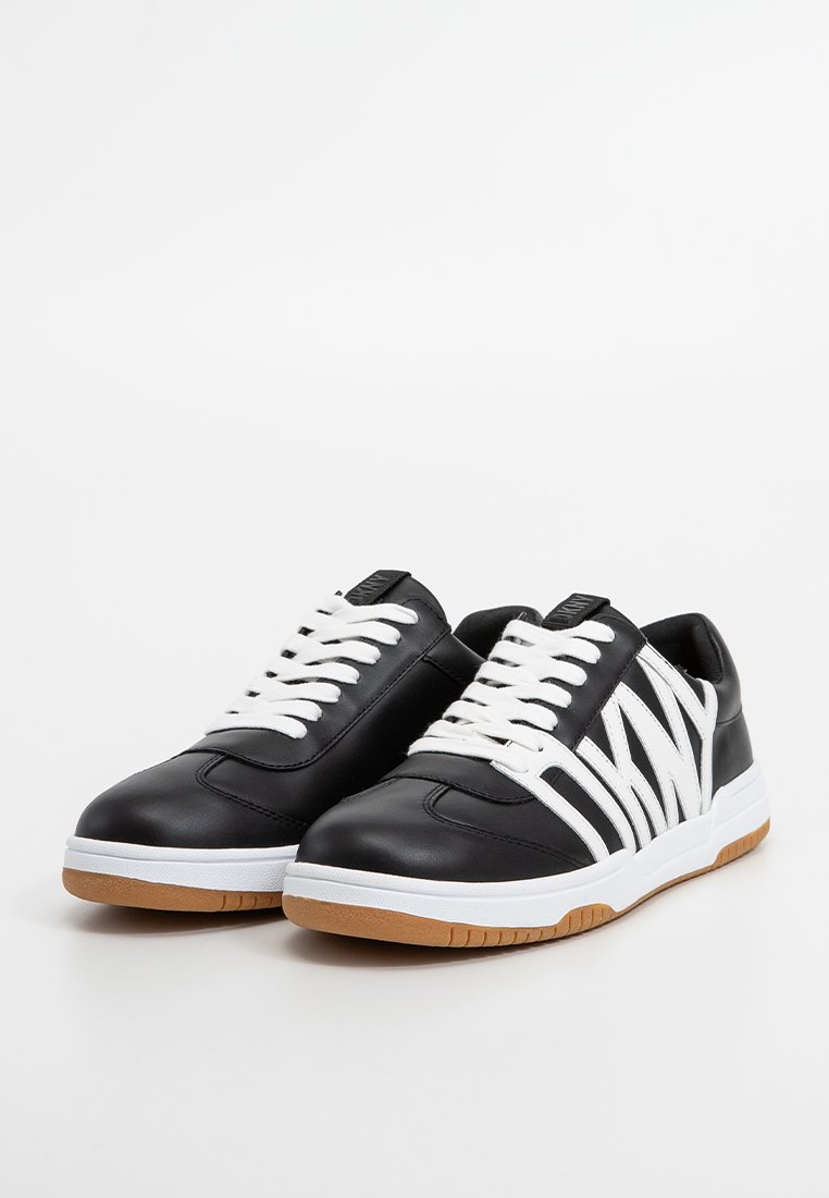 Zapatillas de cuero negro con cordones blancos y un diseño de franjas blancas llamativas. Suela de goma con un agarre texturizado y forma de puntera redondeada.