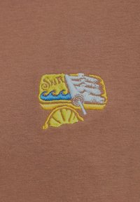 Bruine stof met een textuurfinish, versierd met een kleurrijk geborduurd ontwerp van een strandscène, inclusief golven en een schelp.