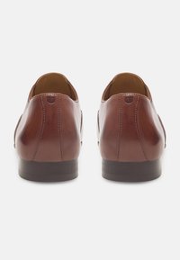 Braune Lederschuhe mit einer glatten Oberfläche, runder Zehenpartie und dunkler, flacher Sohle. Sie verfügen über dezente Nähte und eine kleine Schlaufe an der Ferse.