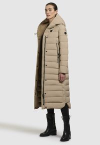 Beige pufferjakke med lang design, oversized krave, lynlås og trykknaplukning, med quiltet tekstur og sidelommer.