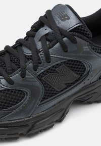 Chaussure de sport noire avec un dessus en mesh, des accents synthétiques texturés et une semelle moulée avec un motif de semelle pour une meilleure adhérence.