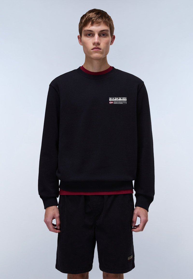 Sort sweatshirt med rød detalje ved halsudskæringen, der har en logo-patch foran. Båret med sorte shorts, sat mod en neutral baggrund.