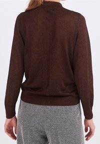 Brun strikket sweater med lange ærmer, der har et subtilt mønster, ribbede manchetter og en løs pasform ved taljen. Mønstrede herringbone bukser er synlige.