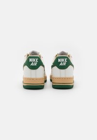 Weiße Leder-Sneaker mit grünen Akzenten, beiger Zwischensohle und grünem Gummi-Außensohle. Mit "NIKE AIR" Branding auf der Ferse.