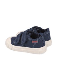 Zapatillas de lona azul marino con suelas de goma blanca, que cuentan con cintas Velcro y costuras blancas en contraste. Etiqueta de logo roja en el lateral.