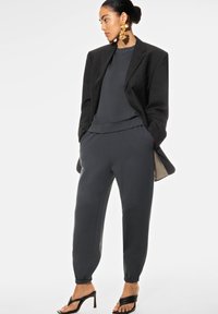 Tummanharmaat, istuvat collegehousut, joissa on resorit nilkoissa, yhdistettynä yhteensopivaan yläosaan ja ylisuurta mustaa bleiseriä. Varustettu kultaisilla näyttävillä korvakoruilla.