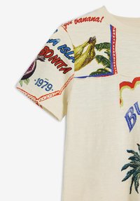 T-shirt i bomull med kort ärm, krämfärgad, med färgglada tryck av bananer och blad samt textdesign i röd och blå.