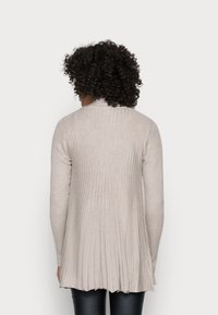 Cardigan côtelé beige clair avec un ourlet évasé et des manches longues, présentant un tissu texturé. Vue de l'arrière avec une finition lisse.