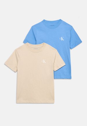 To kortermede t-skjorter med rund hals, en beige og en blå, hver med en liten hvit "cK"-logo på brystet.