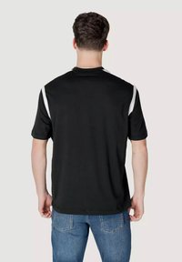 T-shirt nero a maniche corte con accenti bianchi sulle spalle. Tessuto morbido, scollatura rotonda e vestibilità rilassata. Vista posteriore mostrata.