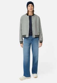 Grau Wollbomberjacke mit schwarz-weißen gestreiften Rippbündchen, kombiniert mit hellblauen weit geschnittenen Jeans und weißen Sneakers.