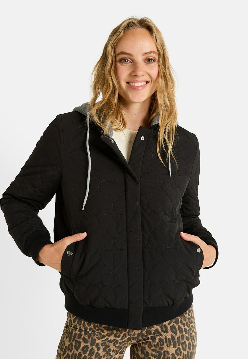 Chaqueta acolchada negra con capucha gris, cierre de botones y bolsillos laterales. Puños y dobladillo acanalados. Combinada con pantalones de estampado de leopardo.