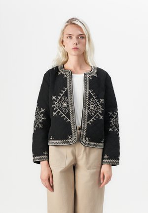 Sort quilted jakke med hvid broderi langs kanterne og blomster mønstre. Designet har en rund halsudskæring og korte ærmer.
