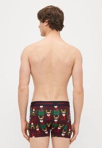 Men's boxer briefs in dark red with a festive reindeer pattern and green plaid. Elastic waistband features "JACK & JONES" logo. Cotton material.