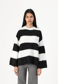 Black and white striped sweater with loose fit, fluffy texture, wide sleeves, and a rounded neckline, paired with gray jeans.