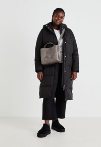 Zwarte lange pufferjas met een rits, gecombineerd met een grijze gestructureerde handtas en zwarte cropped broek. Schoenen zijn zwarte platform schoenen.
