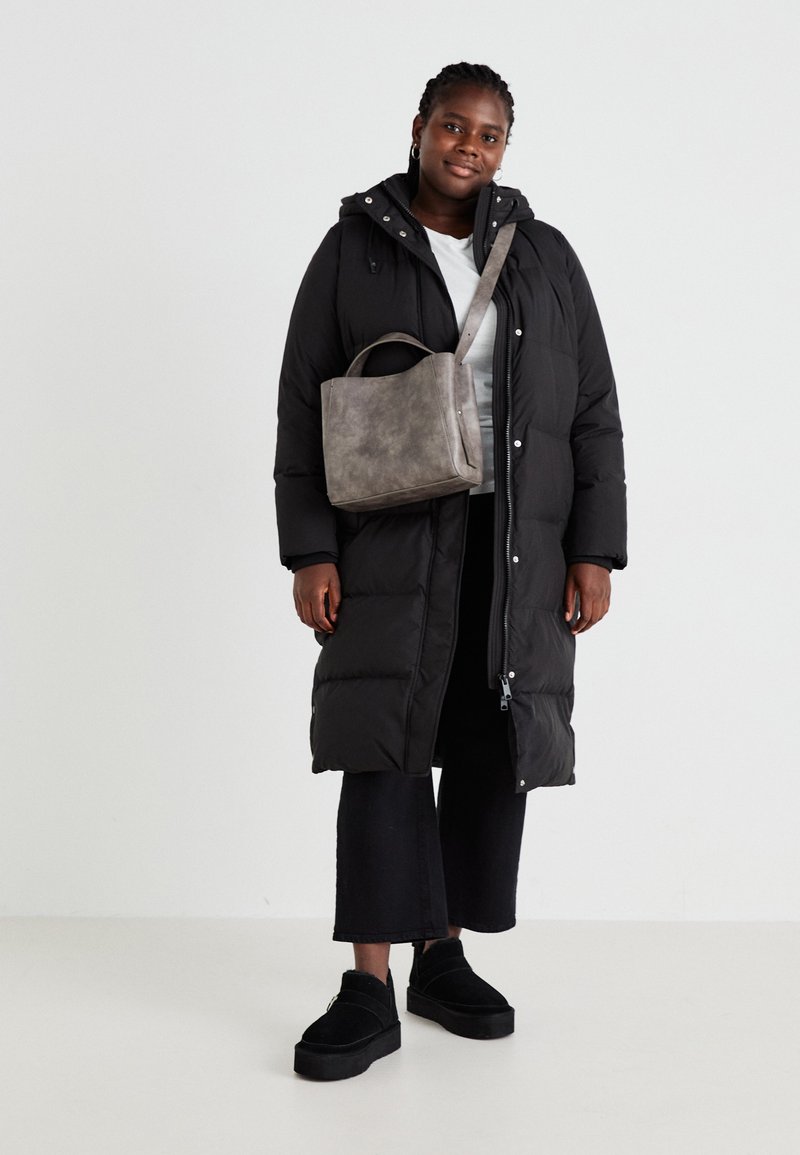 Zwarte lange pufferjas met een rits, gecombineerd met een grijze gestructureerde handtas en zwarte cropped broek. Schoenen zijn zwarte platform schoenen.