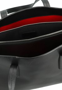 Zwarte leren tote bag met twee handvatten, voorzien van een rode stoffen voering, interne ritszak en zilveren hardware langs de rits.