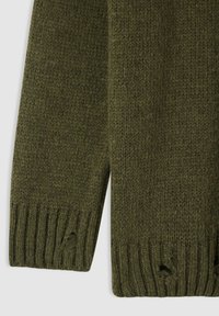 Primo piano delle maniche di un maglione lavorato a maglia verde oliva, con polsini a coste e visibili imperfezioni di pilling.
