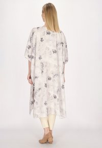 Rochie lungă, fluidă, de culoare crem cu modele florale gri, cu mâneci scurte și o siluetă relaxată, asortată cu colanți bej și încălțăminte.