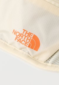 Λευκό ύφασμα με πορτοκαλί λογότυπο "THE NORTH FACE" τυπωμένο κοντά στην ραμμένη άκρη.