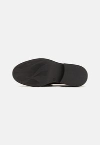 Suela de zapato negra con surcos y curvas texturizadas, hecha de goma. Diseño plano con un acabado suave, que presenta un ligero tacón.