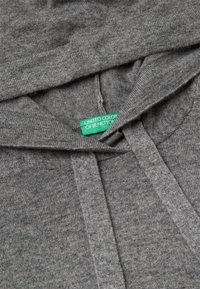 Šedá mikina s kapucí, vybavená šňůrkou a výraznou nášivkou „United Colors of Benetton“ v zelené barvě, vyrobena z měkké, texturované tkaniny.