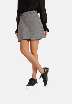 Mini gonna a quadri grigia con vita aderente e orlo svasato, abbinata a sneakers in pelle nera con dettagli dorati e suola bianca.
