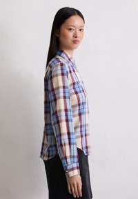 Blauwe, roomkleurige en bordeauxrode geruite blouse met lange mouwen, een kraag en een licht gebogen zoom; gemaakt van een lichte stof.