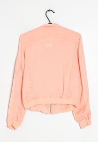 Bomber bunda broskvové barvy s hladkou texturou, s dlouhými rukávy, žebrovanými manžetami, pasem a zipem ve spodní části.