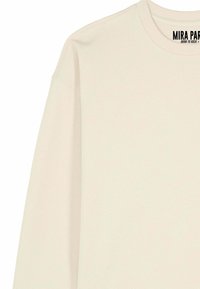 Maglietta a maniche lunghe color crema con scollo girocollo a coste e la scritta "MIRA PARA BORN TO ROCK" stampata all'interno del colletto.