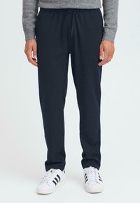 Temno sivi trenirke z elastičnim pasom in vezalko, z stranskimi žepi in sproščenim krojem, v kombinaciji z belimi supergami.