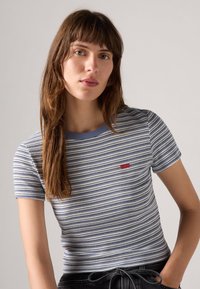 Svītrota īsām piedurknēm veste gaisā zila un balta, ribota tekstūra ar apaļu apkakli, ar mazu sarkanu logotipu uz krūtīm.