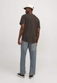 Dunkelgraues Kurzarm-T-Shirt, lockere Passform, kombiniert mit hellblauen geraden Jeans und Schwarz-Weiß-Sneakern. Weißer Cap, rückwärts getragen.
