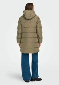 Zelena puffer jakna sa kapuljačom, sa horizontalnim kockastim odeljcima. Uparen sa plavim širokim farmerkama i crnim chunky cipelama.