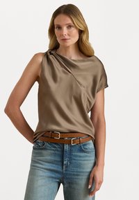 Brun sateng topp med en drapert design og asymmetrisk halsutskjæring, båret over blå denimjeans og et brunt lærbelte.