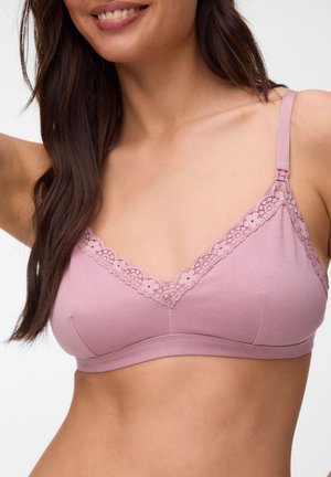 Femme portant un bralette rose clair bordé de dentelle, souriante, avec de longs cheveux foncés et des épaules nues visibles.