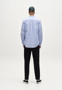 Chemise rayée bleu et blanche à boutons, pantalon noir et baskets noires avec semelles blanches. La chemise possède un col classique et des manches longues.