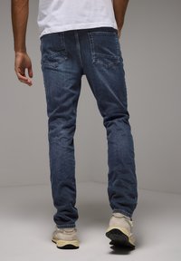 Mörkblå denimjeans med slim fit, med två bakfickor och subtila blekningar. Matchas med ljusfärgade sneakers.