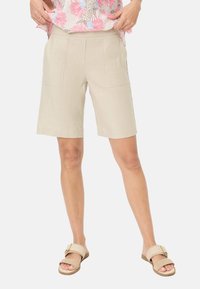 Shorts en lin beige avec poches avant à rabat, longueur genou, et une texture respirante, associés à des sandales glissantes de couleur beige clair.