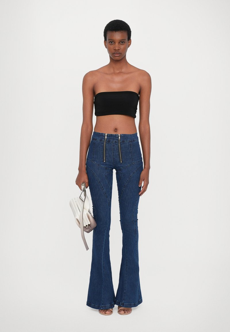 Mörkblå utsvängda jeans med dragkedjefunktioner, texturerad denim, hög midja, i kombination med en svart avtagbar topp och en ljusgrå handväska.